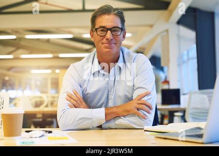 Be the best at what you do. Portrait of a successful businessman posing with his arms crossed at his desk in the office. Stock Photo