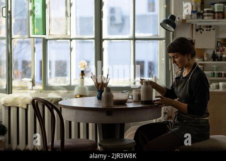 Young skilled lady concentrated on modeling jug from raw clay enjoys hobby creating vase Stock Photo