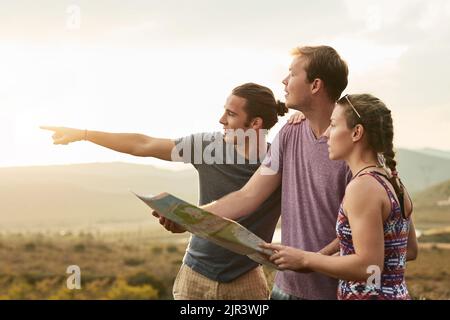 Whats on the other side of that hill. three young hikers consulting a map while exploring a new trail. Stock Photo
