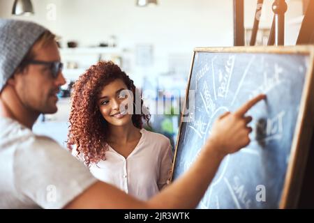 Shes quite impressed with his ideas. two businesspeople discussing their ideas on a blackboard. Stock Photo