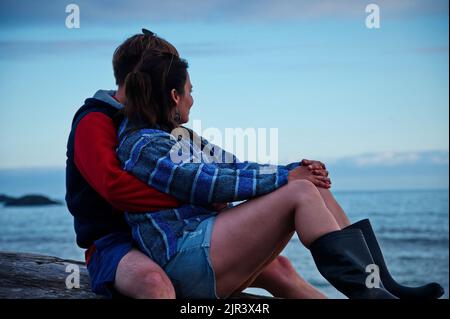 Mature couple sitting on a tree trunk on the beach Stock Photo