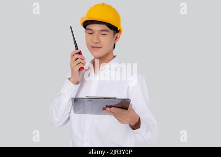 Portrait young asian man is engineer wearing helmet standing and using radio for speak with confident while holding report document isolated on white Stock Photo