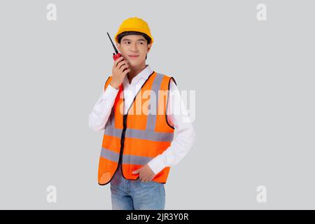Portrait young asian man is engineer wearing helmet standing and using radio for speak with confident isolated on white background, handsome male is a Stock Photo
