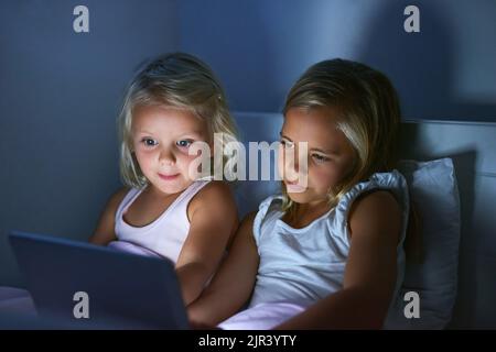 Watching their favourite cartoon before bedtime. two little girls using a digital tablet before bedtime. Stock Photo