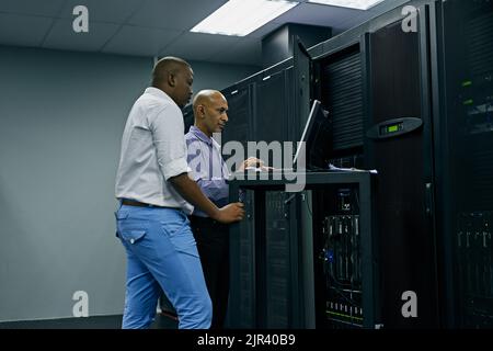 System administrators to the rescue. two IT technicians using a computer while working in a data center. Stock Photo