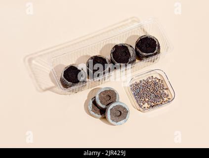 Round Peat briquettes for growing seedlings dry, wet on a beige background and radish seeds in container. Isometric. Stock Photo