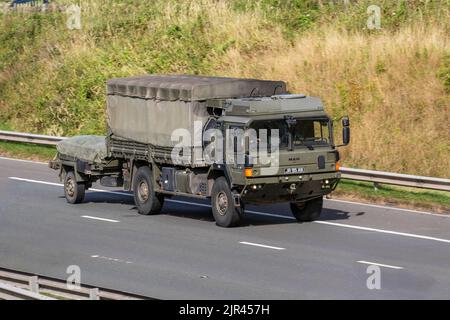 British Army green dropside General Service truck, canvas-covered MAN HX60 18.330 4x4 Military vehicle towing a trailer; travelling on the M6 Motorway UK Stock Photo