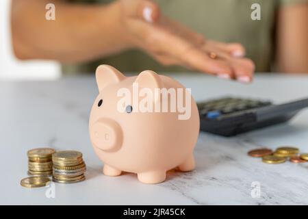 Close-up of a woman's hands counting expenses on a calculator with a piggy bank on an office desk. economy, crisis and inflation. Cost Management Stock Photo