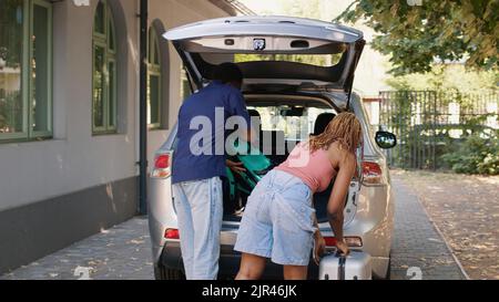 African american couple loading vehicle trunk with voyage luggage while getting ready for holiday citybreak. People putting baggage and trolleys inside car while getting ready for field trip departure Stock Photo