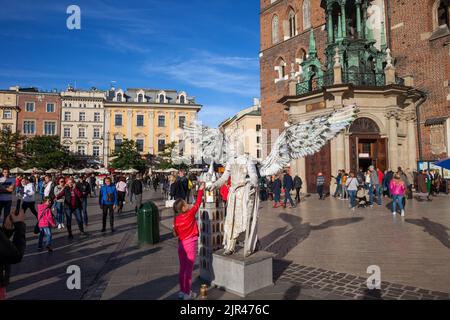 Krakow (Cracow), Poland - September 30, 2018: Group of people and child giving money to angel mime on lively main square in the Old Town in front of S Stock Photo