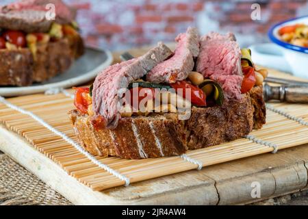 Beef steak on sourdough with garlicky tomatoes, courgettes and cannellini beans Stock Photo