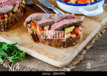 Beef steak on sourdough with garlicky tomatoes, courgettes and cannellini beans Stock Photo