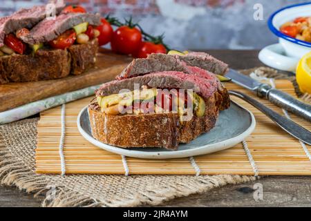 Beef steak on sourdough with garlicky tomatoes, courgettes and cannellini beans Stock Photo