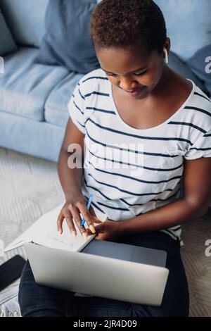 Afro student woman sitting on floor preparing homework or examination in university. Internet application. Stock Photo