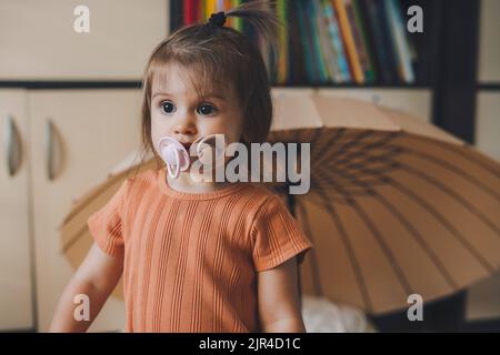 Funny portrait of a baby girl sucking two pacifiers at once and looking to the side. Concept of childhood. New life and parenthood. Stock Photo