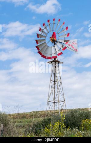 A functioning wind pump, with rotating multi bladed rotor in motion, used to extract water in agriculture in the island of Gozo, Maltese Islands Stock Photo
