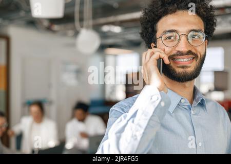 Smiling businessman talking phone standing in office on colleagues background Stock Photo