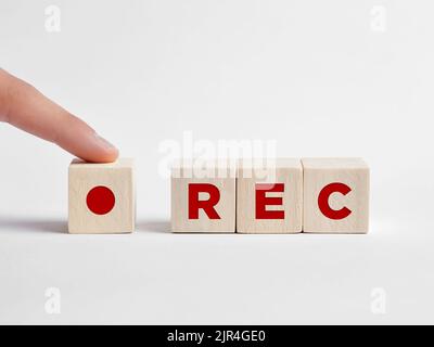 Finger presses the REC record button with the word rec on wooden cubes. Start recording concept. Stock Photo