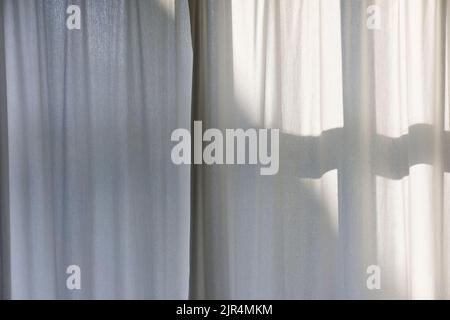 Morning sun shines through white transparent curtains with shadows from the window frame. Stock Photo