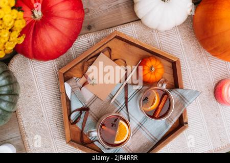 Top view cups with hot spiced tea with star anise, cinnamon stick, slice of orange on the wooden tray with decorative pumpkin, flowers and blank postc Stock Photo