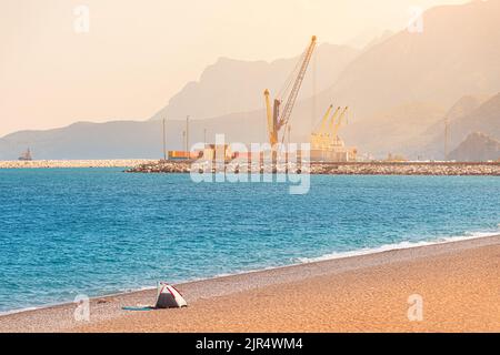 Working construction and industrial cranes at city cargo sea port with ships against mountains background at sunset. Shot taken from Liman beach Stock Photo