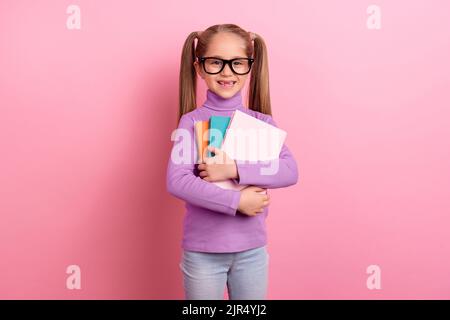 Photo of young little smart schoolgirl go to school for the first time hold copybook isolated on pink color background Stock Photo