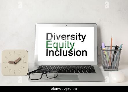 Modern laptop with text DIVERSITY, EQUITY, INCLUSION on screen at workplace Stock Photo