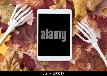 Digital tablet mock-up with monster skeleton hands and autumn leaves background. Happy Halloween, online shopping, studying, sales mockup. Fall flat lay, top view. Internet application template Stock Photo