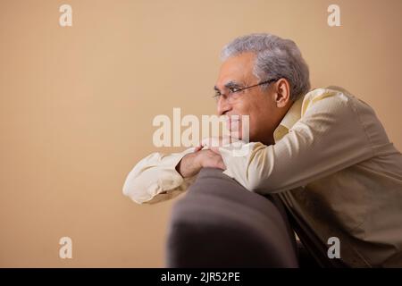 Senior man looking away while leaning on sofa Stock Photo