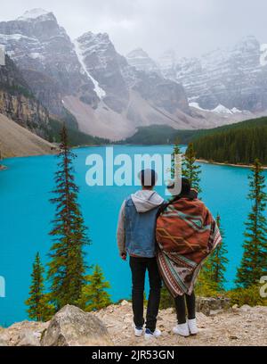 Lake moraine during a cold snowy day in Canada, turquoise waters of the Moraine lake with snow. Banff National Park of Canada Canadian Rockies. Young couple men and women standing by the lake Stock Photo