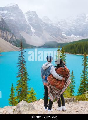 Lake moraine during a cold snowy day in Canada, turquoise waters of the Moraine lake with snow. Banff National Park of Canada Canadian Rockies. Young couple men and women standing by the lake Stock Photo