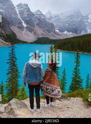 Lake moraine during a cold snowy day in Canada, turquoise waters of the Moraine lake with snow. Banff National Park of Canada Canadian Rockies. Young couple men and women standing by the lake Stock Photo