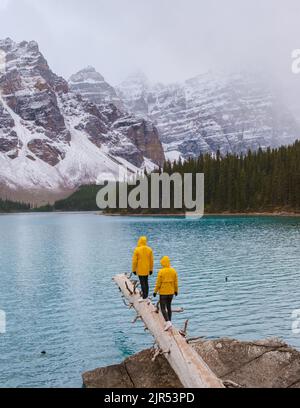 Lake moraine during a cold snowy day in Autumn in Canada, Beautiful turquoise waters of the Moraine lake with snow. couple of men and women in yellow raincoat jacket during snow Stock Photo