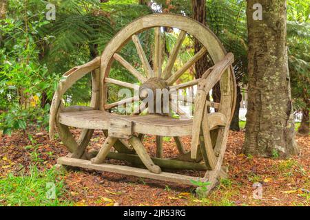 A rustic wooden seat made out of an old wagon wheel, sitting in a woodland garden Stock Photo