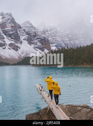 Lake moraine during a cold snowy day in Autumn in Canada, Beautiful turquoise waters of the Moraine lake with snow. couple of men and women in yellow raincoat jacket during snow Stock Photo