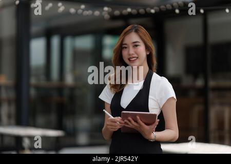 Beautiful Asian women Barista smiling and using tablet at her cafe Stock Photo
