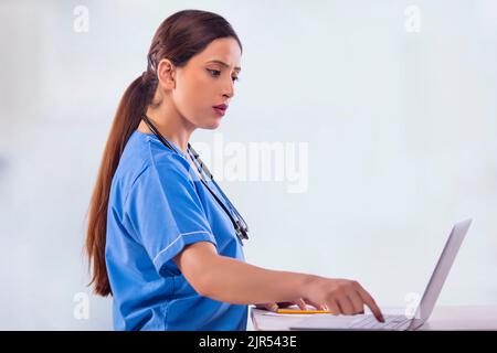 Portrait of female nurse in blue scrub working on laptop. Stock Photo