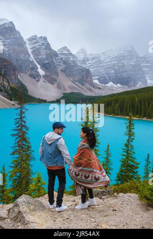 Lake moraine during a cold snowy day in Canada, turquoise waters of the Moraine lake with snow. Banff National Park of Canada Canadian Rockies. Young couple men and women standing by the lake Stock Photo