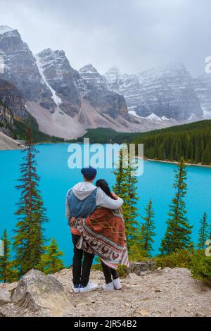 Lake moraine during a cold snowy day in Canada, turquoise waters of the Moraine lake with snow. Banff National Park of Canada Canadian Rockies. Young couple men and women standing by the lake Stock Photo