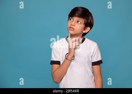 Portrait of a thoughtful boy standing against blue background Stock Photo