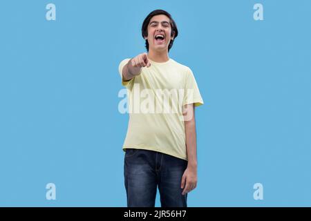 Portrait of a teenage boy pointing towards camera while standing against blue background Stock Photo