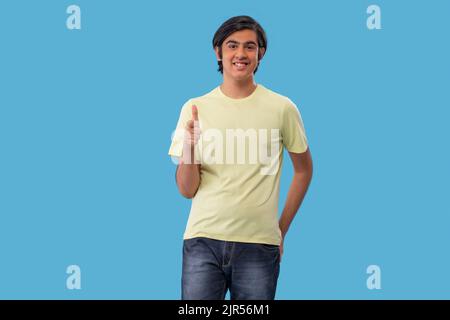 Portrait of a teenage boy pointing towards camera while standing against blue background Stock Photo