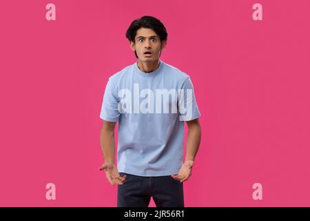 Portrait of a shocked teenage boy gesturing while standing against pink background Stock Photo