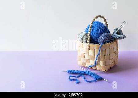 Blue balls of knitting threads on a lilac background in a basket with knitting needles Stock Photo