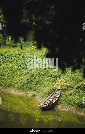 A vertical shot of a small boat on the river bank spotted from the bottom of a tree Stock Photo