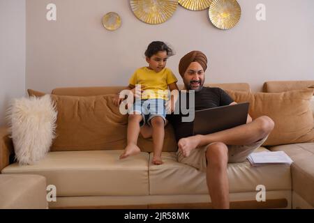 Father and daughter watching cartoons on laptop in living room Stock Photo