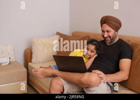 Father and daughter watching cartoons on laptop in living room Stock Photo