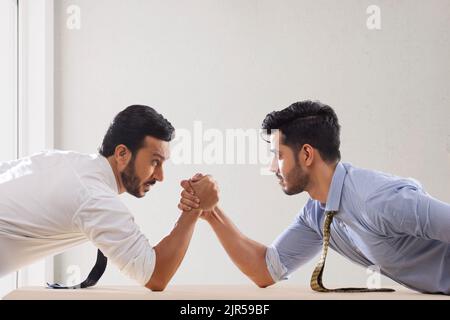 Corporate employees in formal clothing engaged in an arm wrestling match. Stock Photo