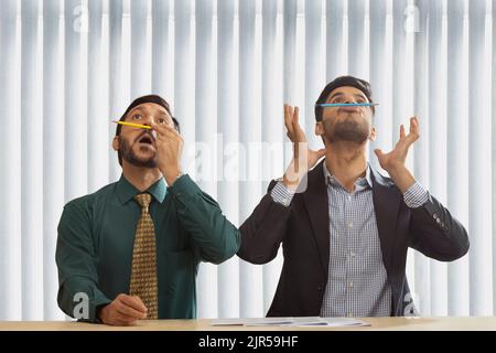 Corporate co-workers sitting together and balancing pencils on their nose. Stock Photo