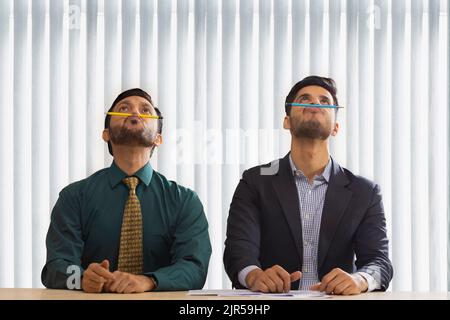 Corporate co-workers sitting together and balancing pencils on their nose. Stock Photo